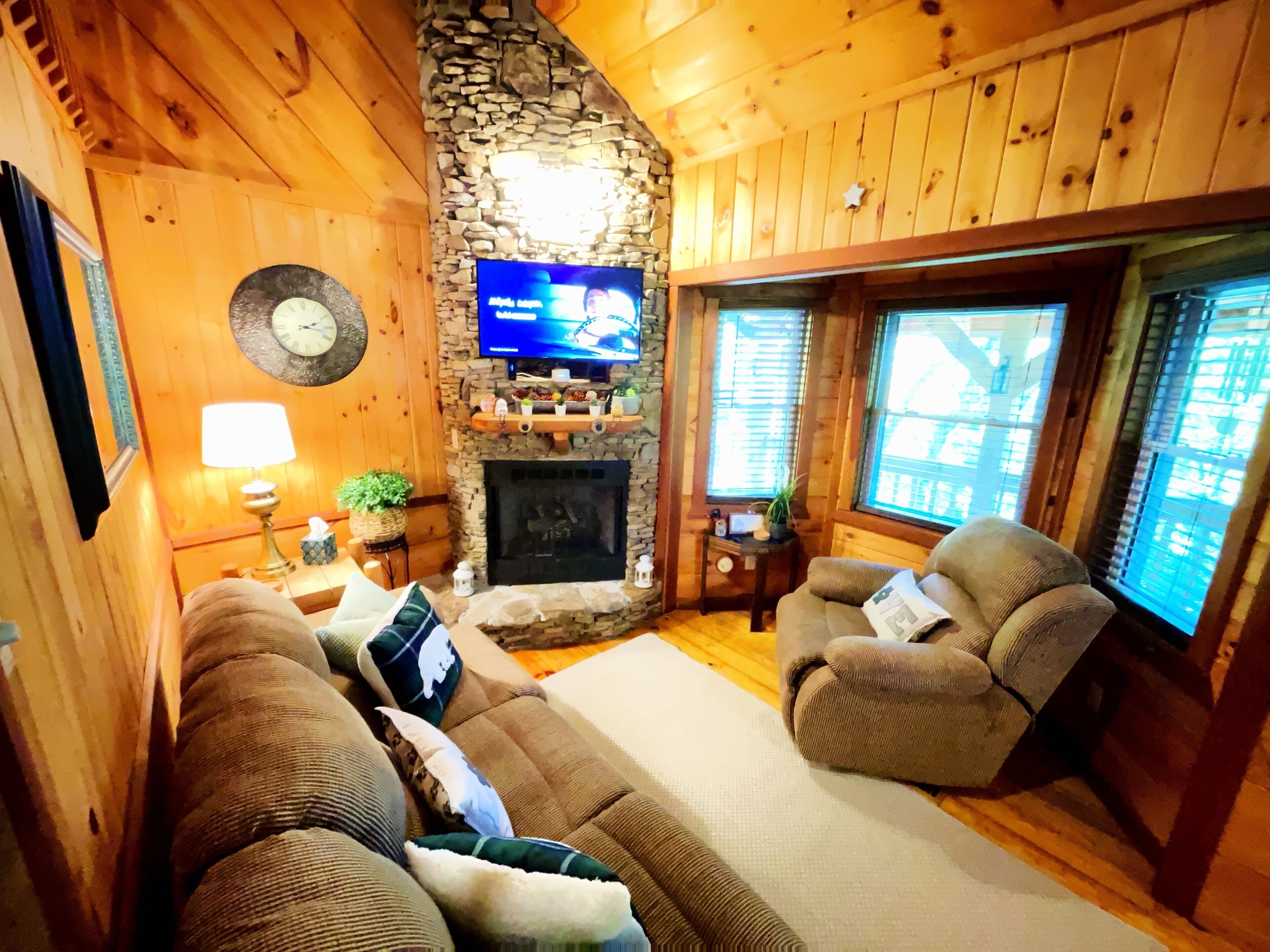 A cozy living room with a stone fireplace, wooden walls, a television, and comfortable seating.