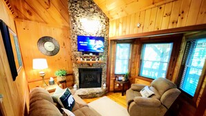 Ein gemütliches Wohnzimmer mit Kamin aus Stein, Holzwänden, einem Fernseher und bequemen Sitzmöglichkeiten.