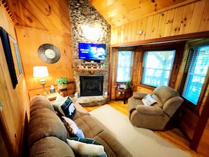 A cozy living room with a stone fireplace, wooden walls, a television, and comfortable seating.