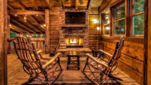 A cozy cabin interior with a stone fireplace, wooden walls, and rocking chairs. - Stress Free Summit - Mountain Views | Hot Tub | Outdoor Fireplace | Gas Grill (Blue Ridge)