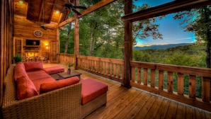 A wooden deck with a sofa and a fireplace, overlooking a forested landscape. - Stress Free Summit - Mountain Views | Hot Tub | Outdoor Fireplace | Gas Grill (Blue Ridge)