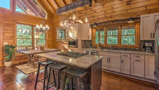 A spacious kitchen with wooden beams, large windows, and a central island with bar stools. - Stress Free Summit - Mountain Views | Hot Tub | Outdoor Fireplace | Gas Grill (Blue Ridge)