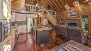 A spacious cabin with a high ceiling, wooden interior, a kitchen with modern appliances, a fireplace, and a cozy seating area. - Stress Free Summit - Mountain Views | Hot Tub | Outdoor Fireplace | Gas Grill (Blue Ridge)