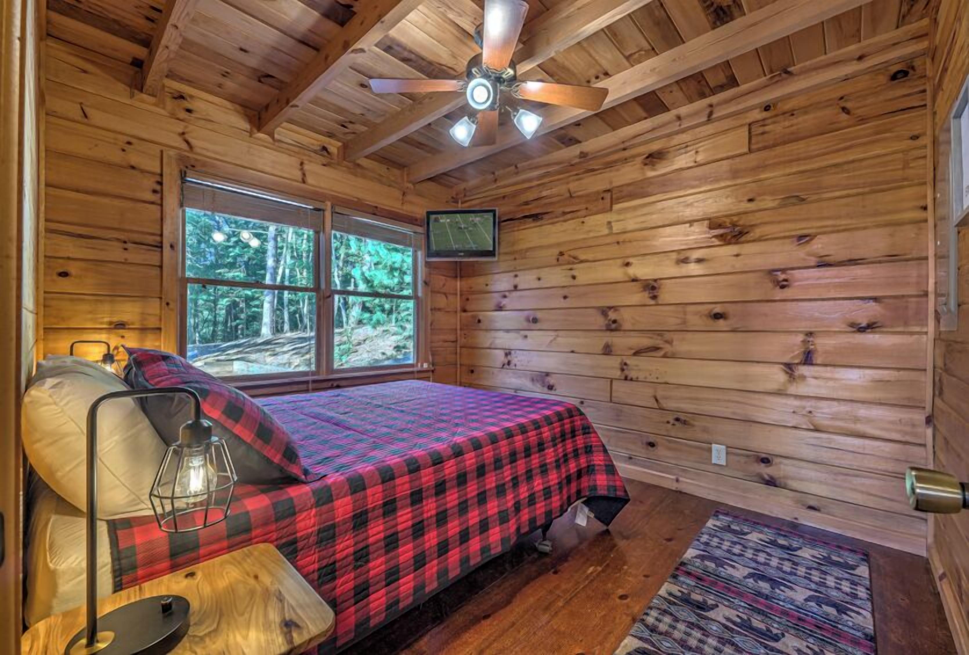A cozy cabin bedroom with a bed, a television, and a ceiling fan.
