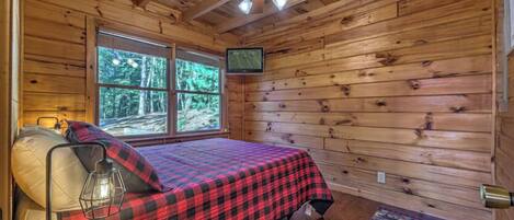 A cozy cabin bedroom with a bed, a television, and a ceiling fan.