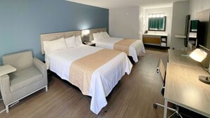 A hotel room with two beds, a desk, a chair, a TV, and a bathroom with a mirror and sink.
