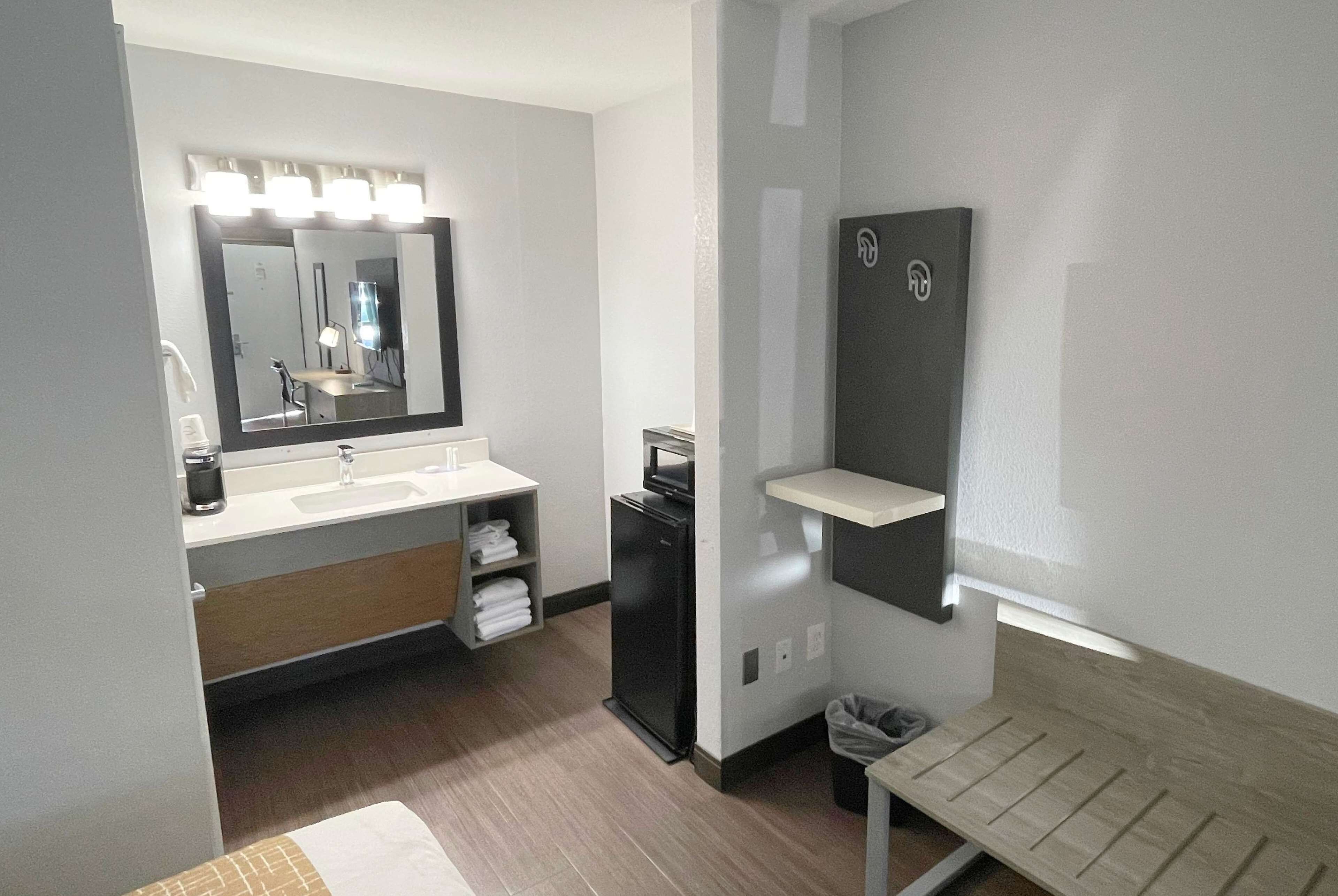 A modern bathroom with a large mirror, vanity, and a small refrigerator.
