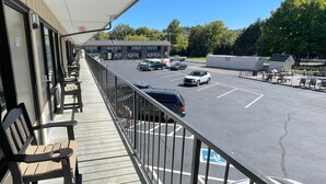 A balcony with outdoor seating, a parking lot with several cars, and a building in the background.
