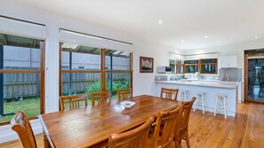 A modern kitchen with a central island, wooden dining table, and chairs. - Ideal family home a just a stones through from the popular Little East Beach (Port Fairy)
