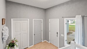 Un corridoio con tre porte bianche, una luce a soffitto e vista su un giardino tramite una porta in vetro.