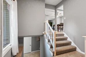 A staircase with carpeted steps and white railings, leading to a dining area with chairs and a table.