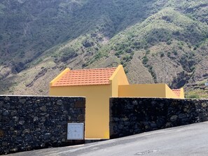 Un bâtiment jaune avec un toit rouge, un mur en pierre et un paysage montagneux en arrière-plan.