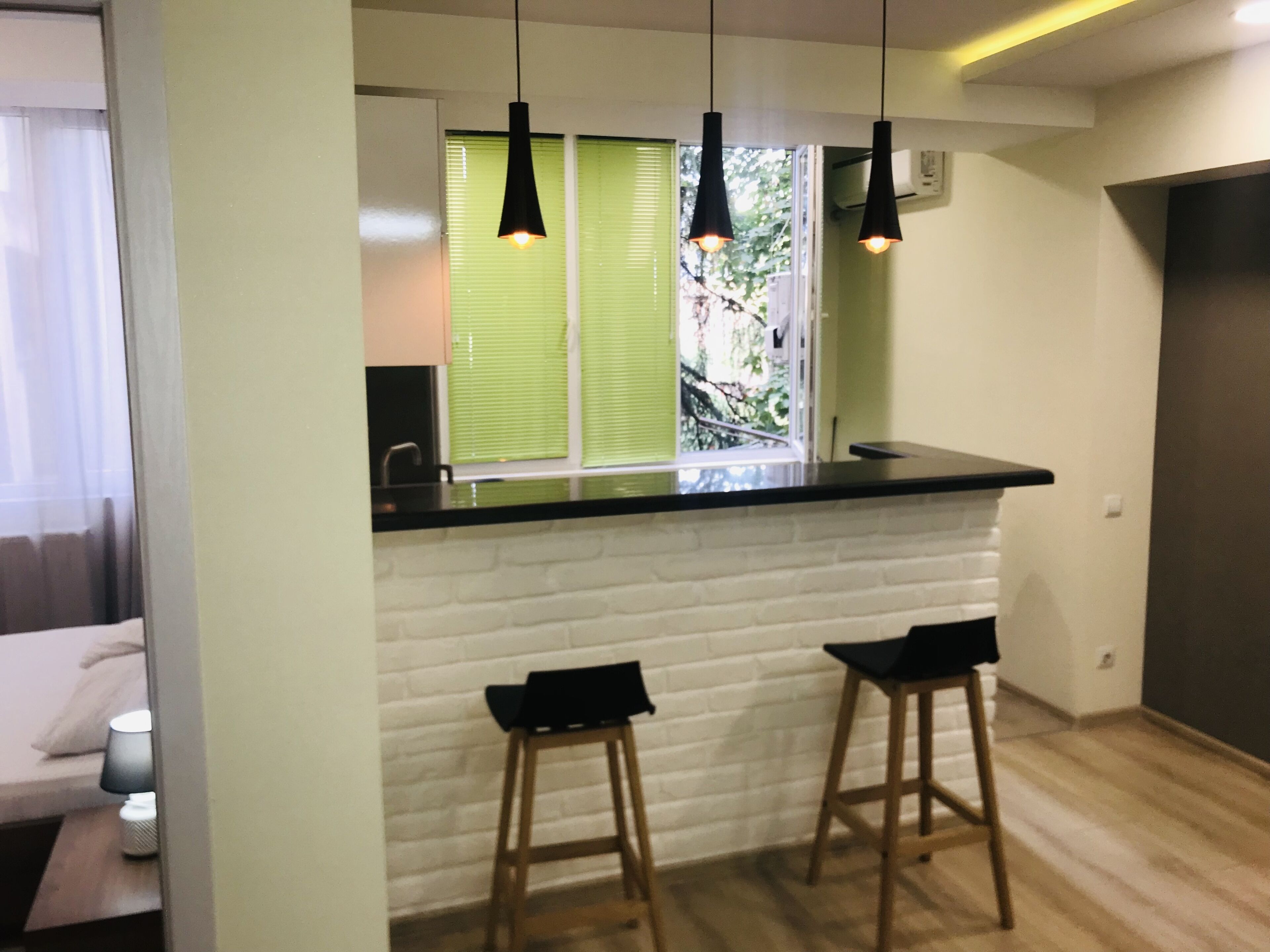 A kitchen with a white brick backsplash, two black pendant lights, and a window with green blinds.