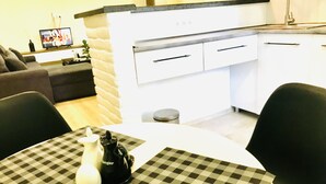 Una cocina moderna con armarios blancos, encimera negra y un comedor con una alfombrilla de cuadros y una jarrón blanco.