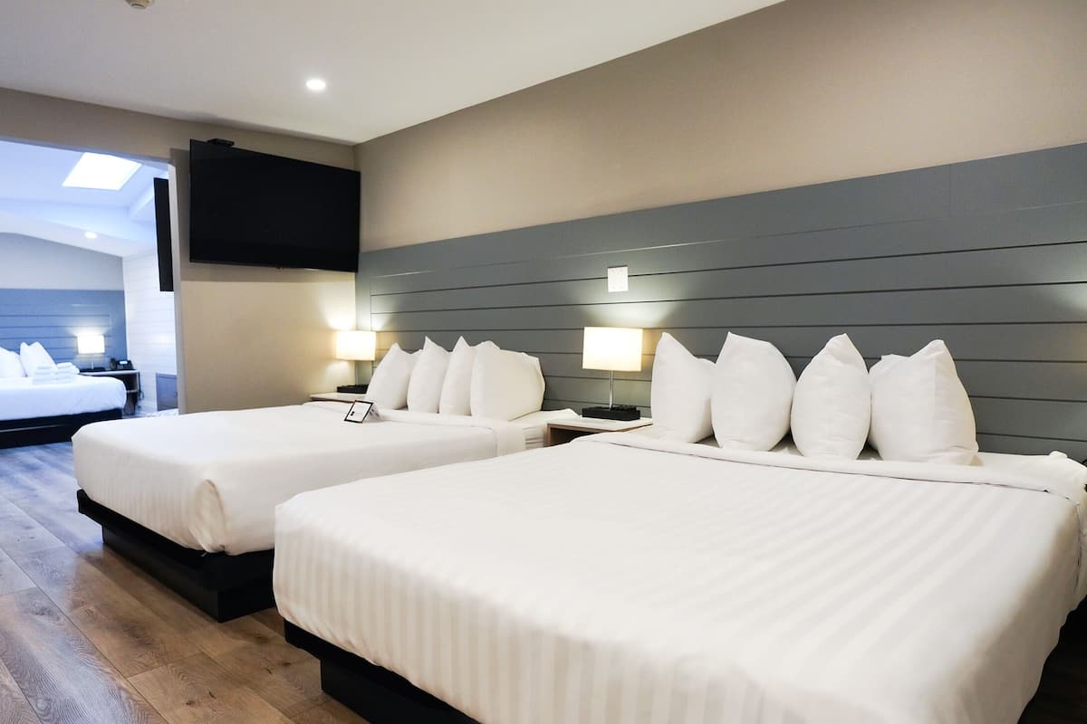 Une chambre d’hôtel avec deux lits, un téléviseur fixé au mur et une vue sur la mer, visible à travers une porte vitrée.