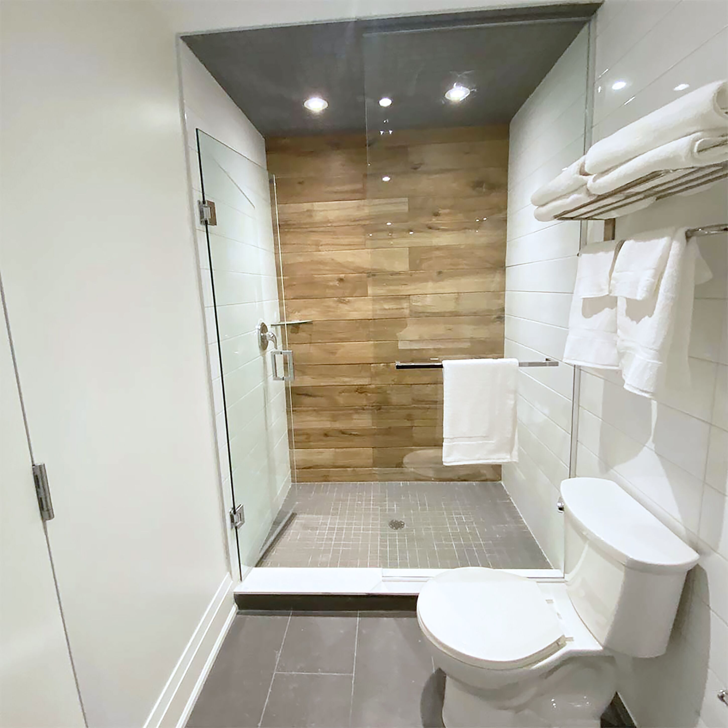A modern bathroom with a glass shower enclosure, a white toilet, and a wooden wall.