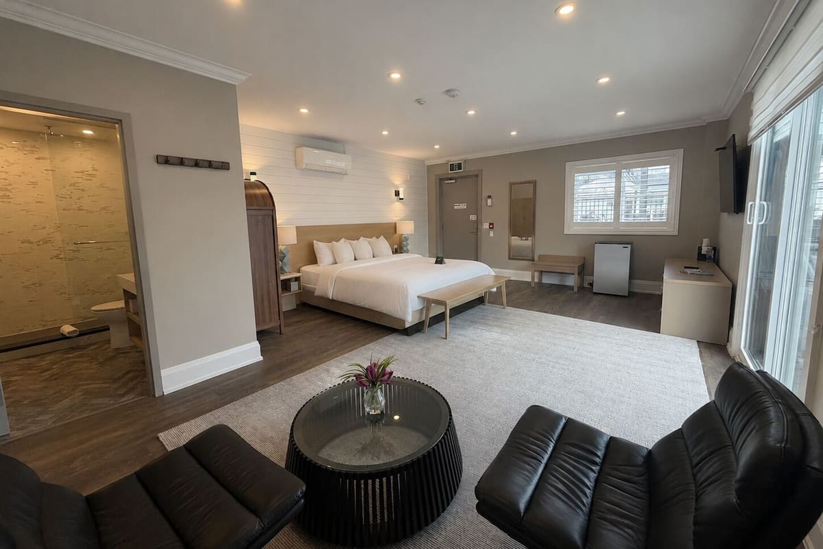 Une chambre d’hôtel moderne dotée d’un grand lit, d’un coin salon avec une table basse, d’un petit bureau et d’une salle de bain avec douche et toilettes.