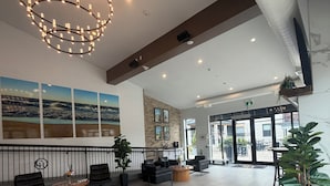 A spacious lobby with a modern chandelier, seating area, and a large window with a view of the beach. - Colonial Hotel & Suites  (Lambton Shores)