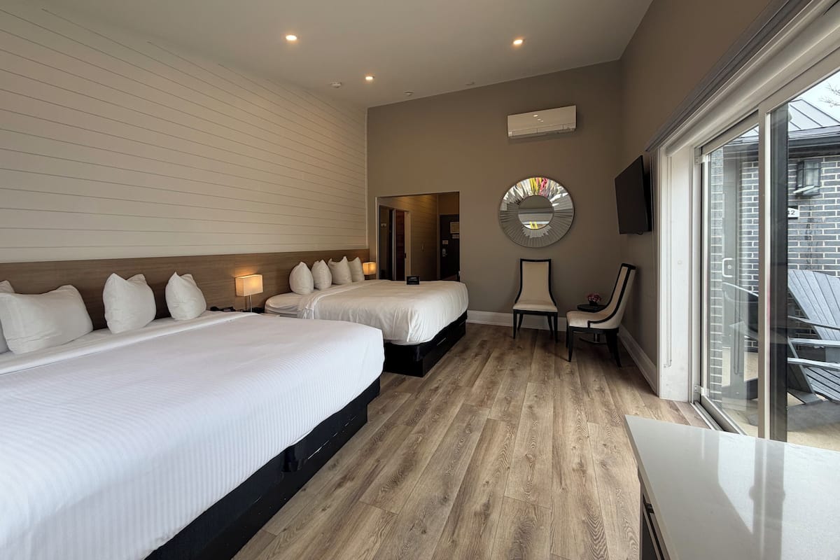 Une chambre d’hôtel avec deux lits, une chaise, un miroir rond et une grande fenêtre.