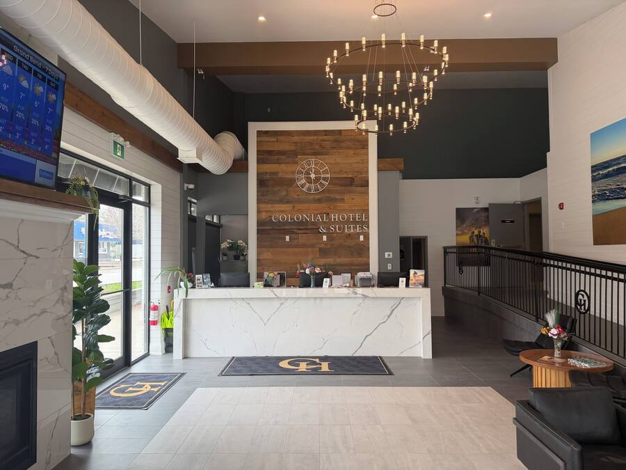 Zona de recepción de hotel con mostrador de mármol, pared decorativa de madera, candelabro y vistas al exterior.