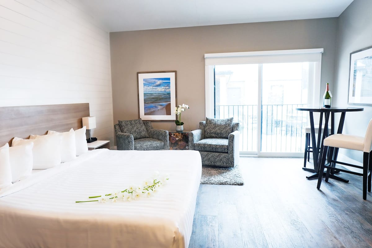 Une chambre d’hôtel avec un grand lit, deux fauteuils, une petite table et un balcon avec vue.