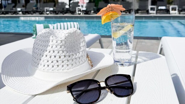 A poolside table with a white hat, sunglasses, and a glass of water with a lemon slice and an umbrella. - Colonial Hotel & Suites  (Lambton Shores)