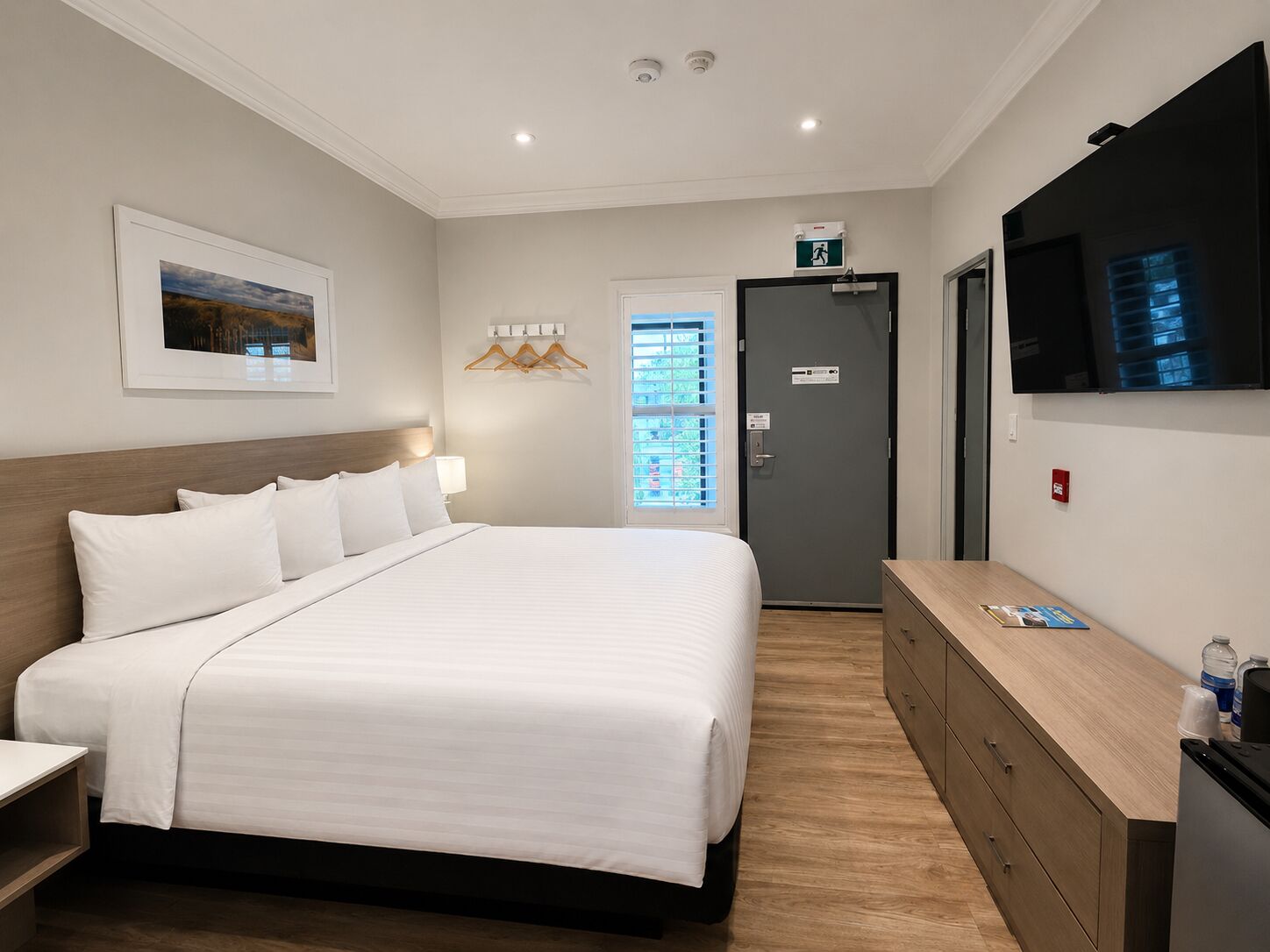 A hotel room with a bed, bedside table, dresser, and a TV on the wall.
