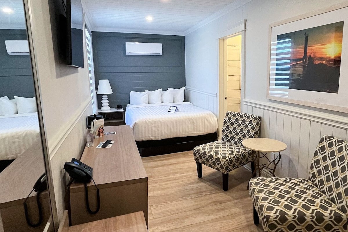 Une chambre d’hôtel avec deux lits, un bureau, une chaise, une petite table, un téléviseur et un tableau encadré au mur.