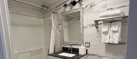A modern bathroom with a white sink, mirror, and toilet. There is a shower curtain and a towel rack with towels.
