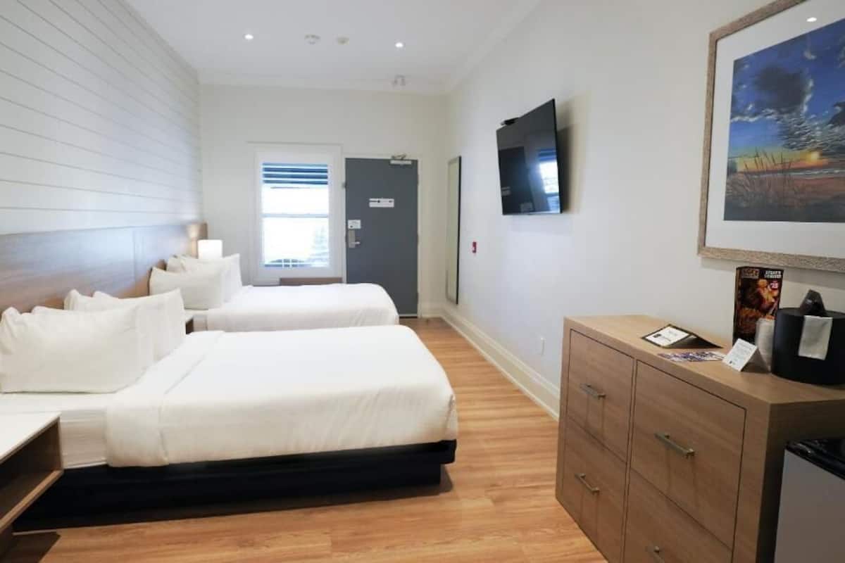 Une chambre d’hôtel avec deux lits, une télévision, un tableau et une armoire en bois.