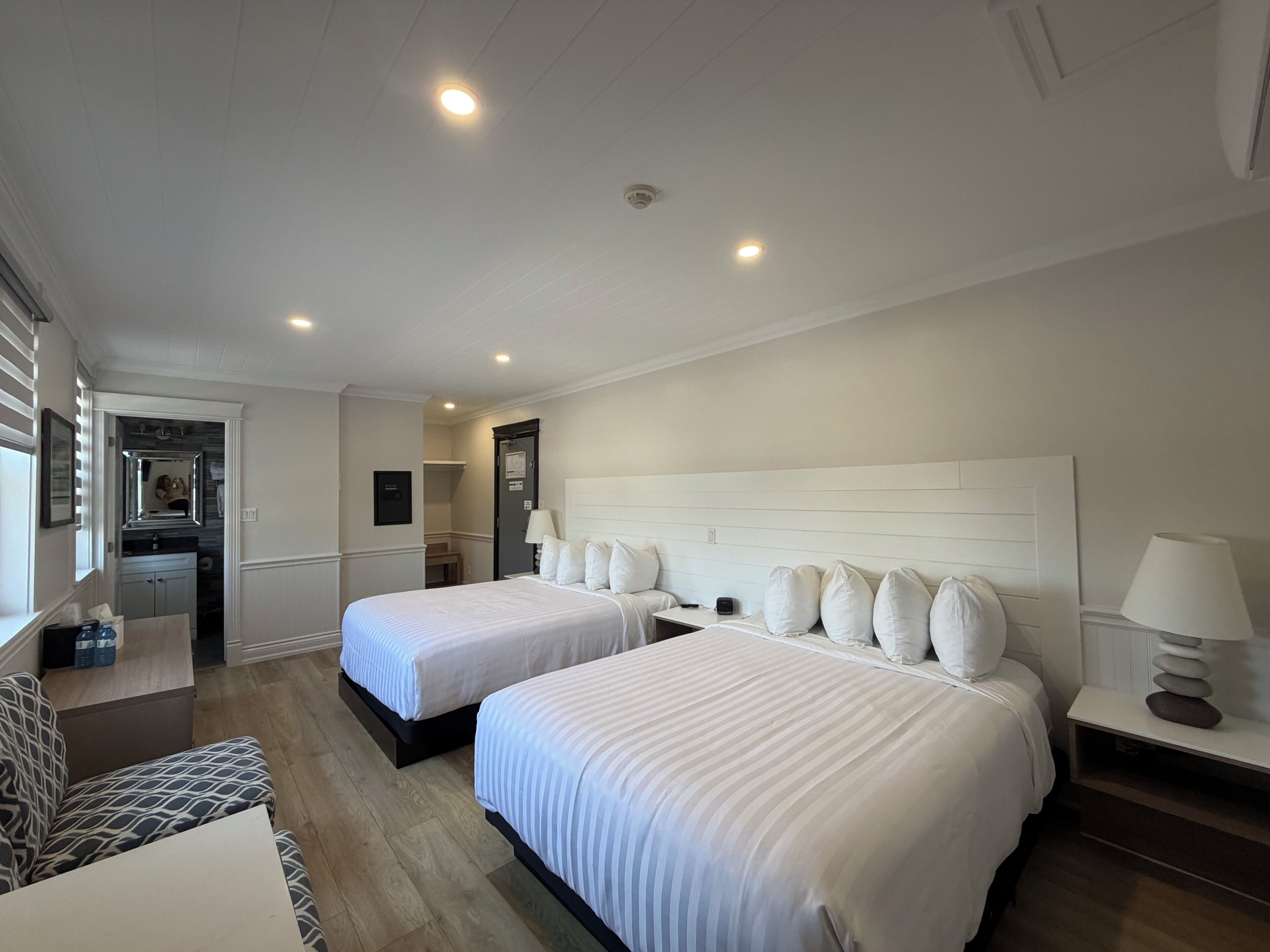 A hotel room with two beds, a desk, a chair, a mirror, and a wardrobe.