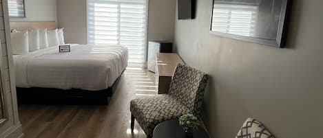 A modern hotel room with a large bed, a sofa, a small table, and a TV mounted on the wall.