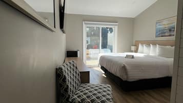 Habitación de hotel moderna con una cama, una silla, una mesita con una planta y vistas al exterior a través de una puerta corredera.