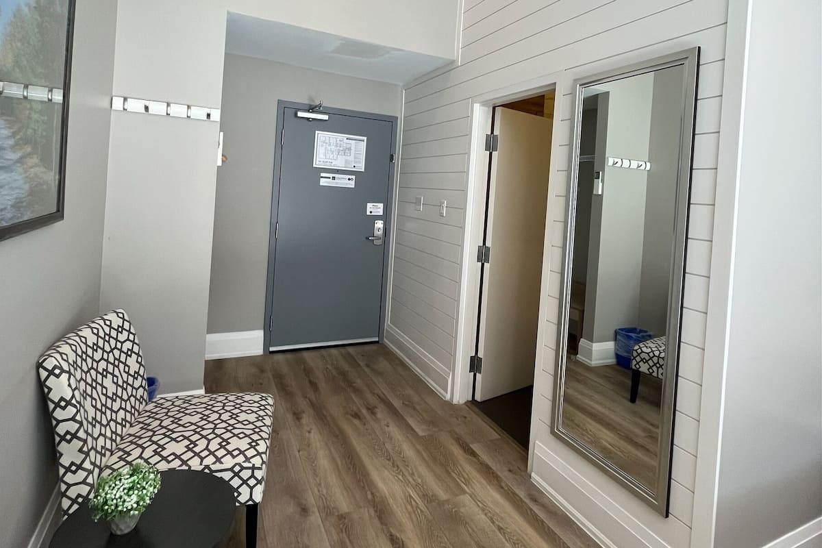 Un intérieur moderne avec un plancher en bois, un fauteuil à motifs, une petite table et un grand miroir.