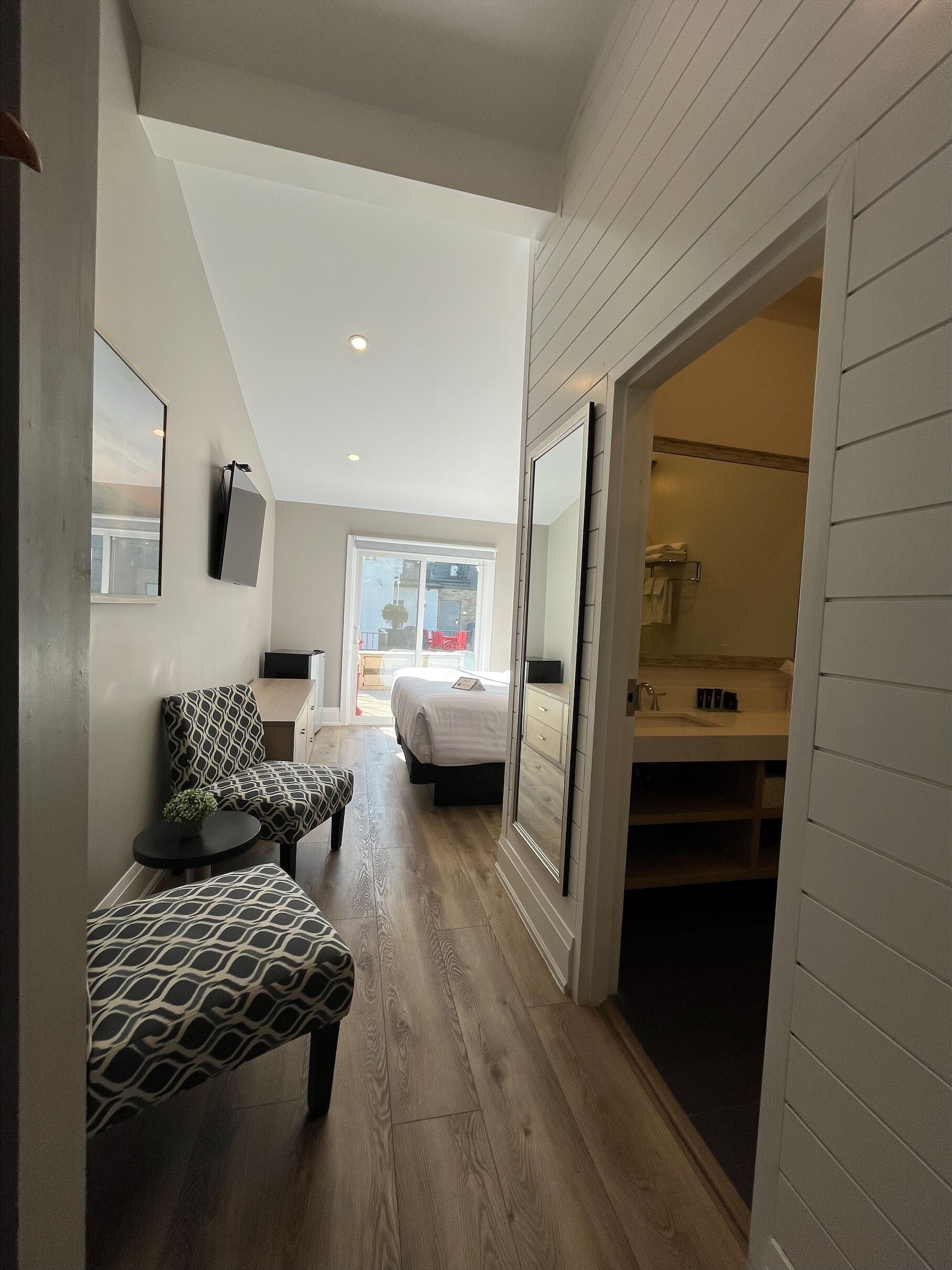 Un dormitorio moderno con una cama grande, una zona de estar con sillones estampados y un vestidor.