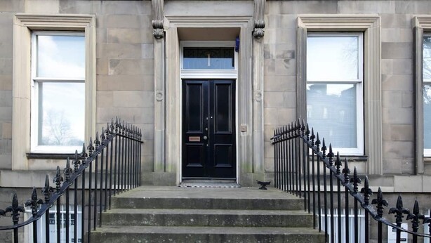A building facade with a central entrance, flanked by two large windows, and a symmetrical black iron railing on the steps. - Quirky, West End, Georgian Apartment (Edinburgh)