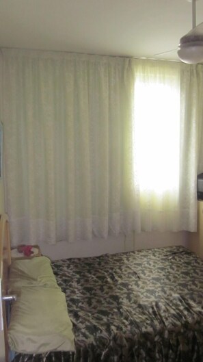 A room with a bed, a wooden headboard, a window with sheer curtains, and a ceiling fan. - 2-bedroom apartment 50 meters from Praia do Forte Beach. (Cabo Frio)