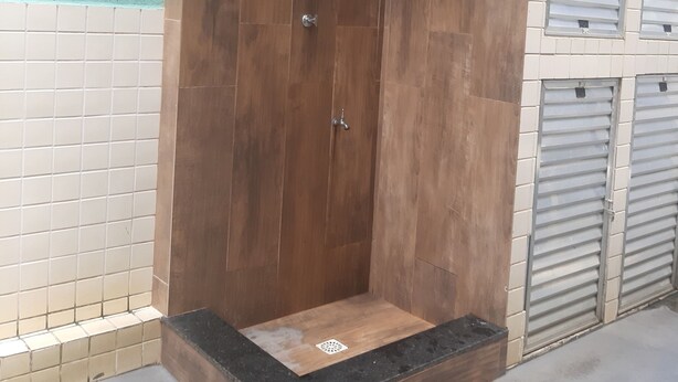 Une cabine de douche en bois avec un plan de travail noir et une pomme de douche en métal.