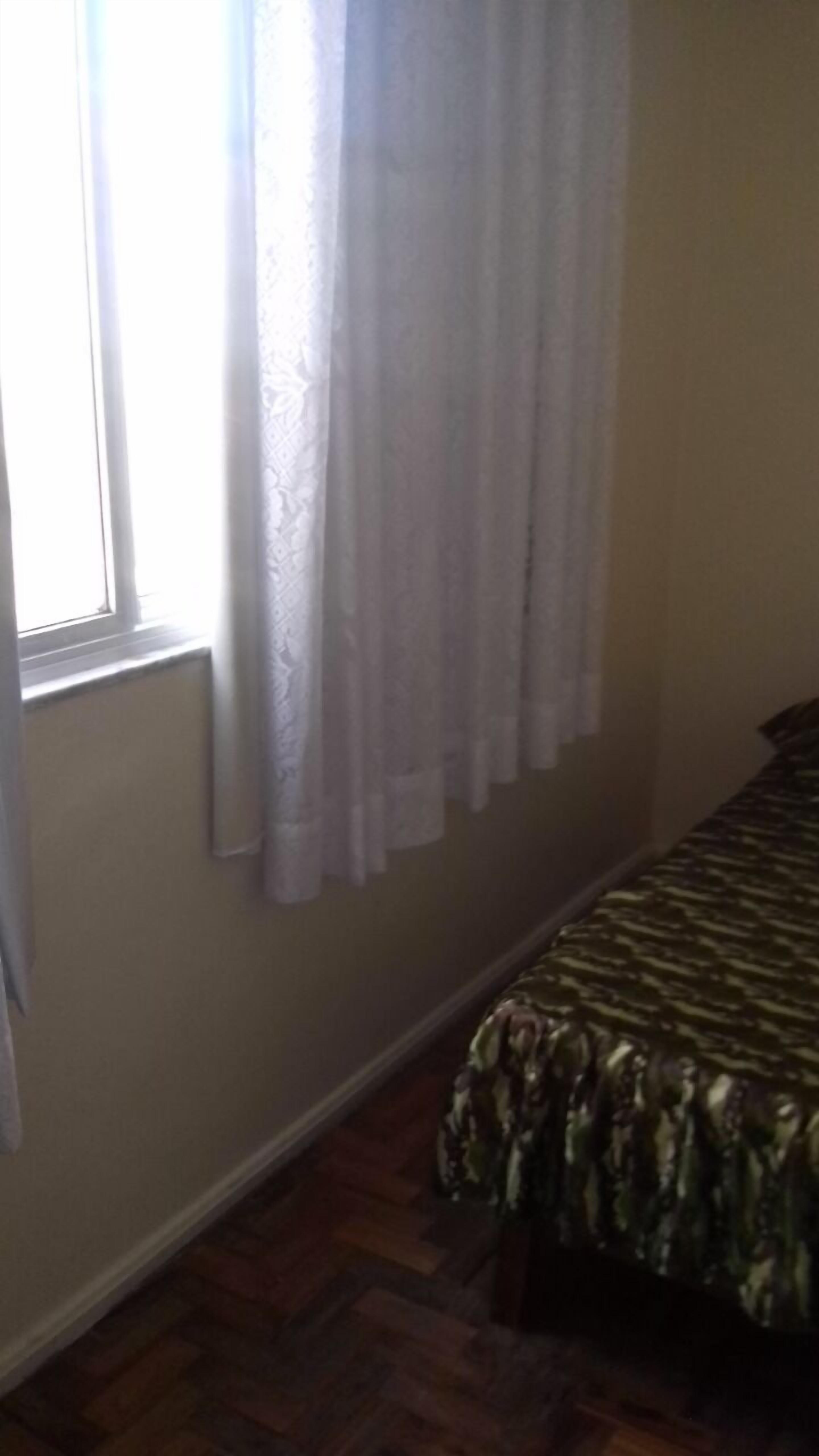 Une chambre avec un lit, une fenêtre avec des rideaux blancs et un radiateur.