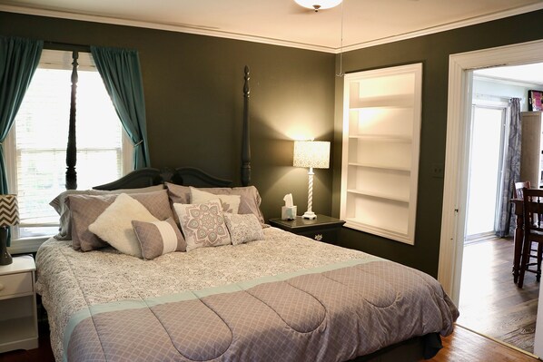 Um quarto com uma cama, mesa de cabeceira, luminária e janela com cortinas.