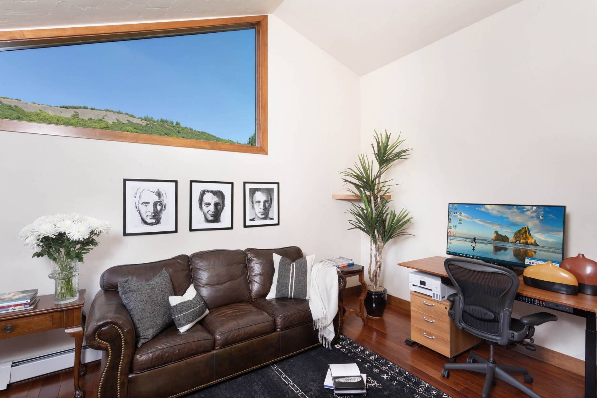 Un espace de bureau moderne avec un canapé en cuir, un bureau doté d’un ordinateur et des œuvres d’art encadrées accrochées au mur.