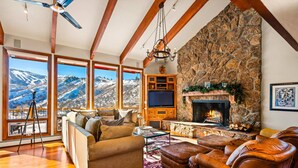 Un salon chaleureux avec une cheminée en pierre, des canapés en cuir et une grande fenêtre donnant sur un paysage montagneux enneigé.