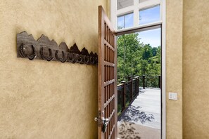 Une porte en bois avec un portail en métal, un crochet en métal en forme de fer à cheval fixé au mur, et une vue sur une terrasse en bois et la verdure à l’extérieur.