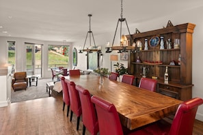 A spacious dining area with a large wooden table and red chairs, a wooden cabinet with decorative items, and a view of a grassy outdoor area.