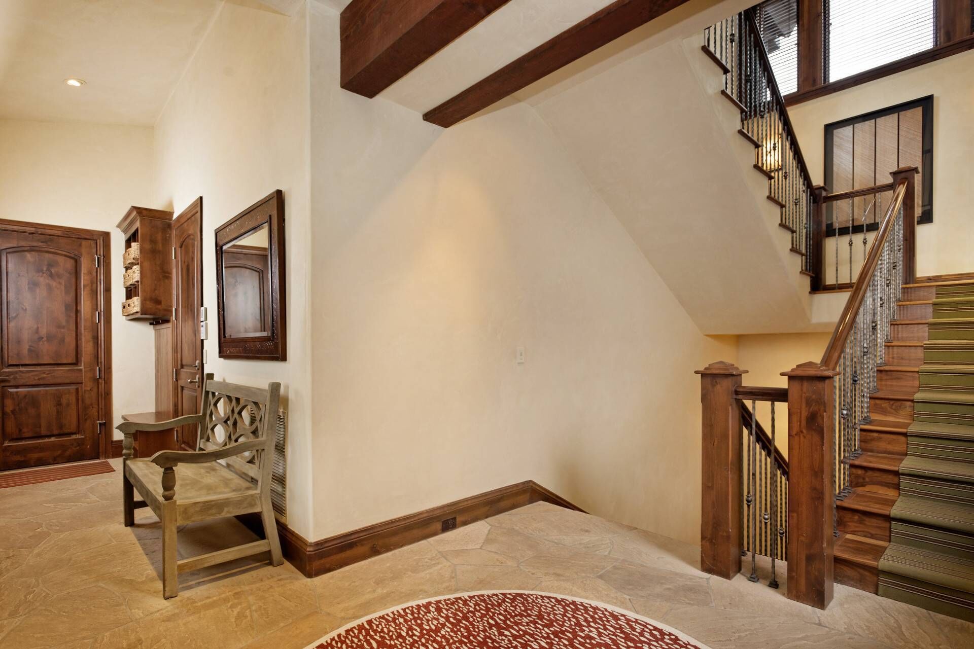 A spacious foyer with a wooden staircase, a bench, and a large mirror.