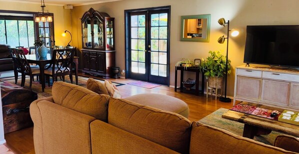 A living room with a sofa, dining table, chairs, a cabinet, a television, and a large window.