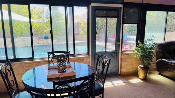 A sunlit patio with a round table, chairs, and a potted plant. - Gated Hacienda Retreat •Large Pool & Spa •Pet Friendly• Near Beaches & SeaWorld (San Diego)
