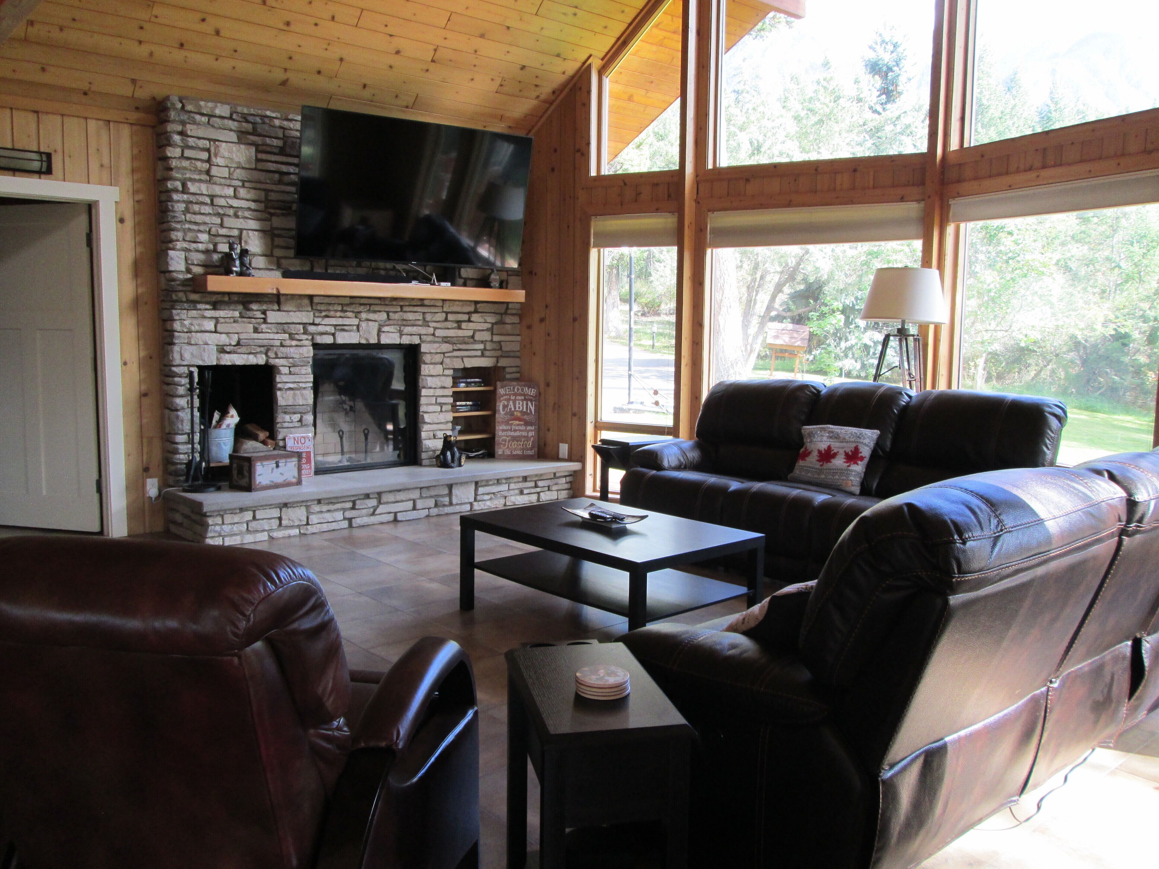 Una sala de estar acogedora con chimenea de piedra, muebles de cuero y ventanas amplias con vistas al exterior.