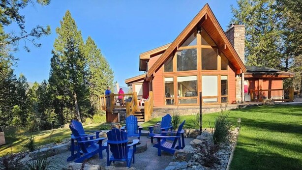Een lodge met een grote houten constructie, een terras met blauwe stoelen en een stenen pad.