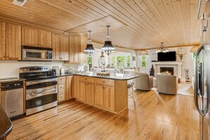 Enjoy cooking in this well-equipped kitchen with a large island, stainless steel appliances, and a fireplace in the background.